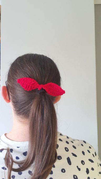A hairband with a mini bow attached in someones hair in the colour red