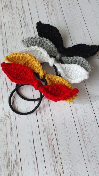A hairband with a mini crochet bow in red, yellow, white, grey and black
